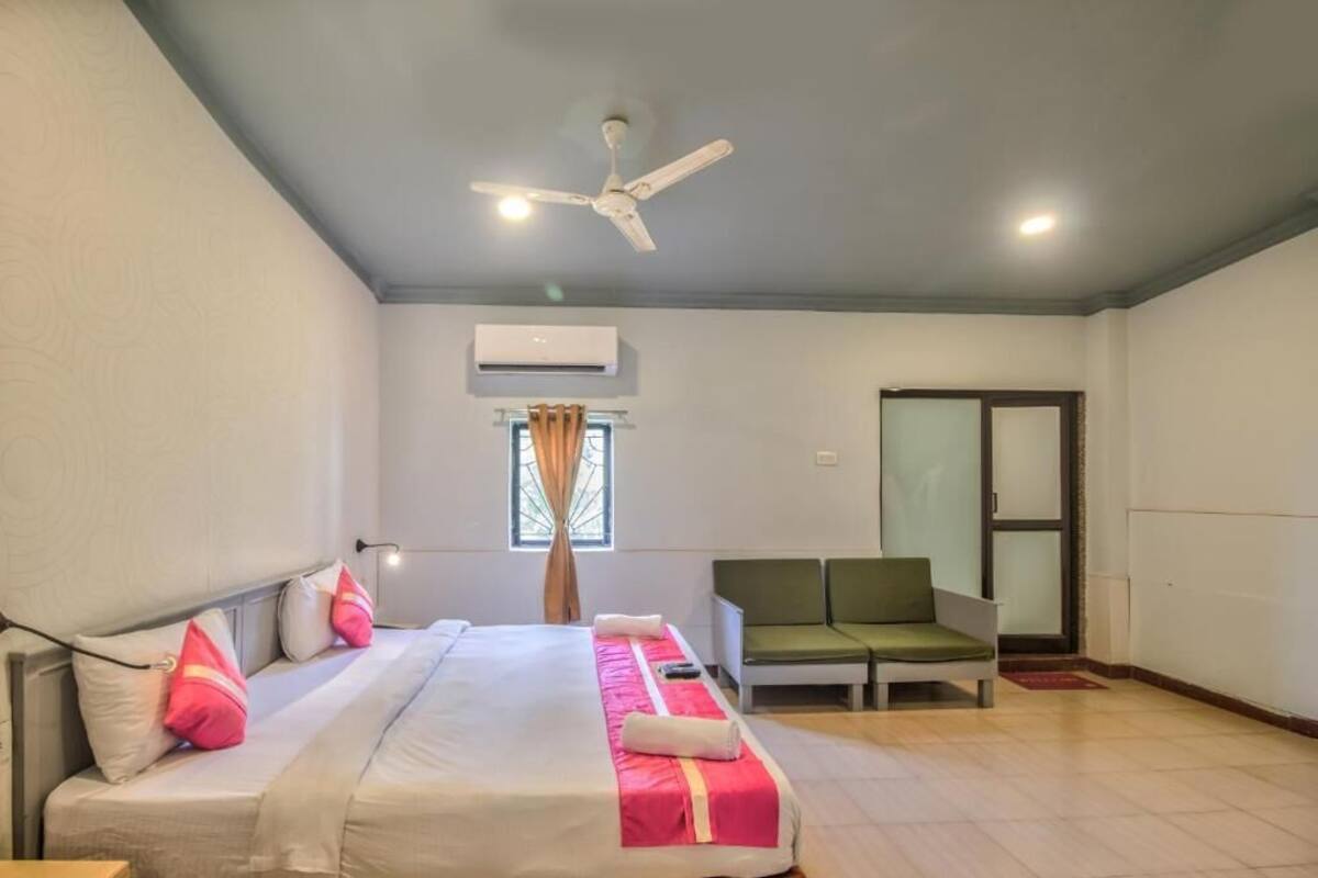 A hotel room with a bed, a green sofa, a ceiling fan, and an air conditioning unit.