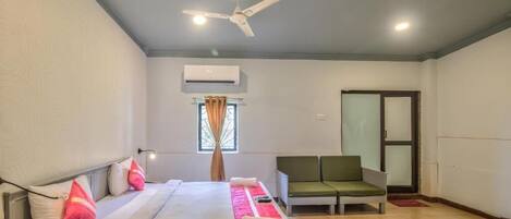 A hotel room with a bed, a green sofa, a ceiling fan, and an air conditioning unit.