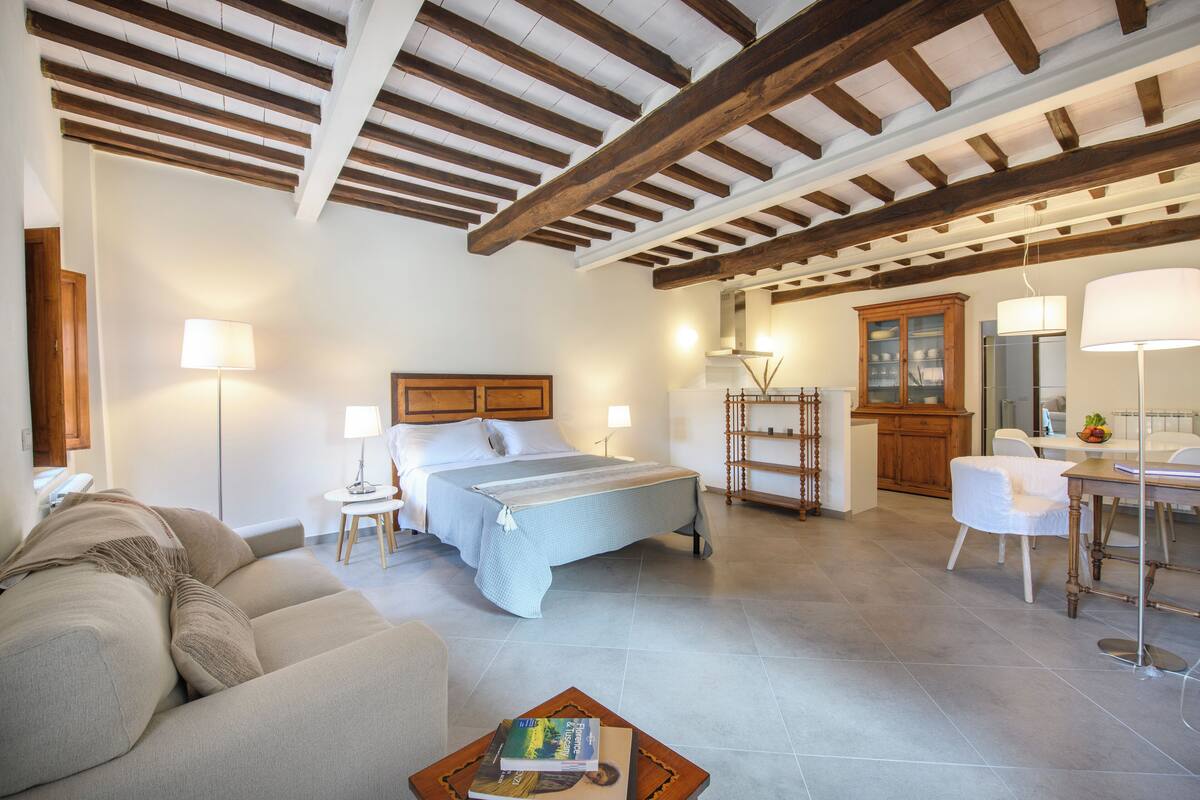 Un dormitorio con cama, mesitas de noche, un aparador de madera y un área de comedor con mesa y sillas.
