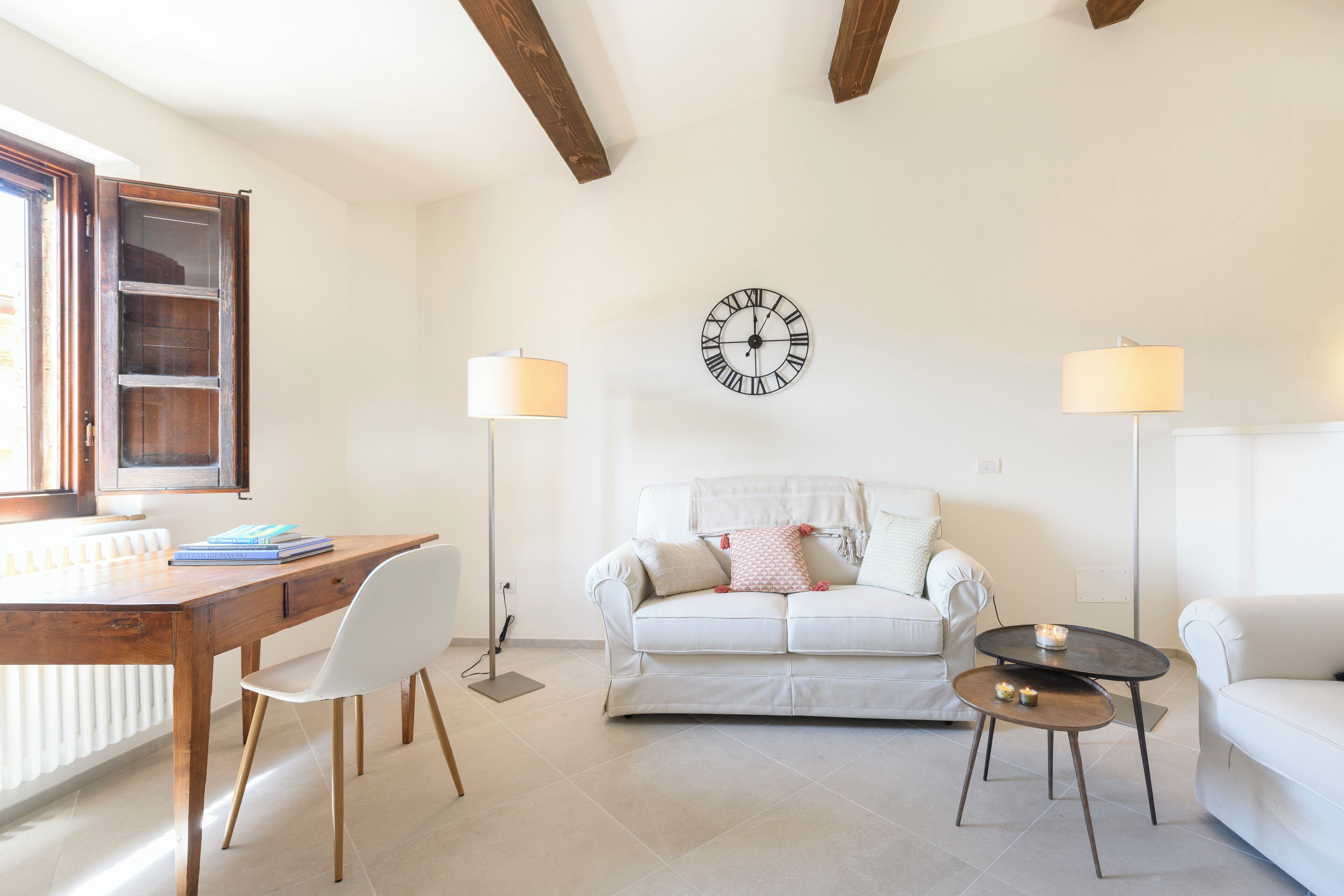 Een woonkamer met een houten bureau, een witte stoel, een witte bank en twee vloerlampen.