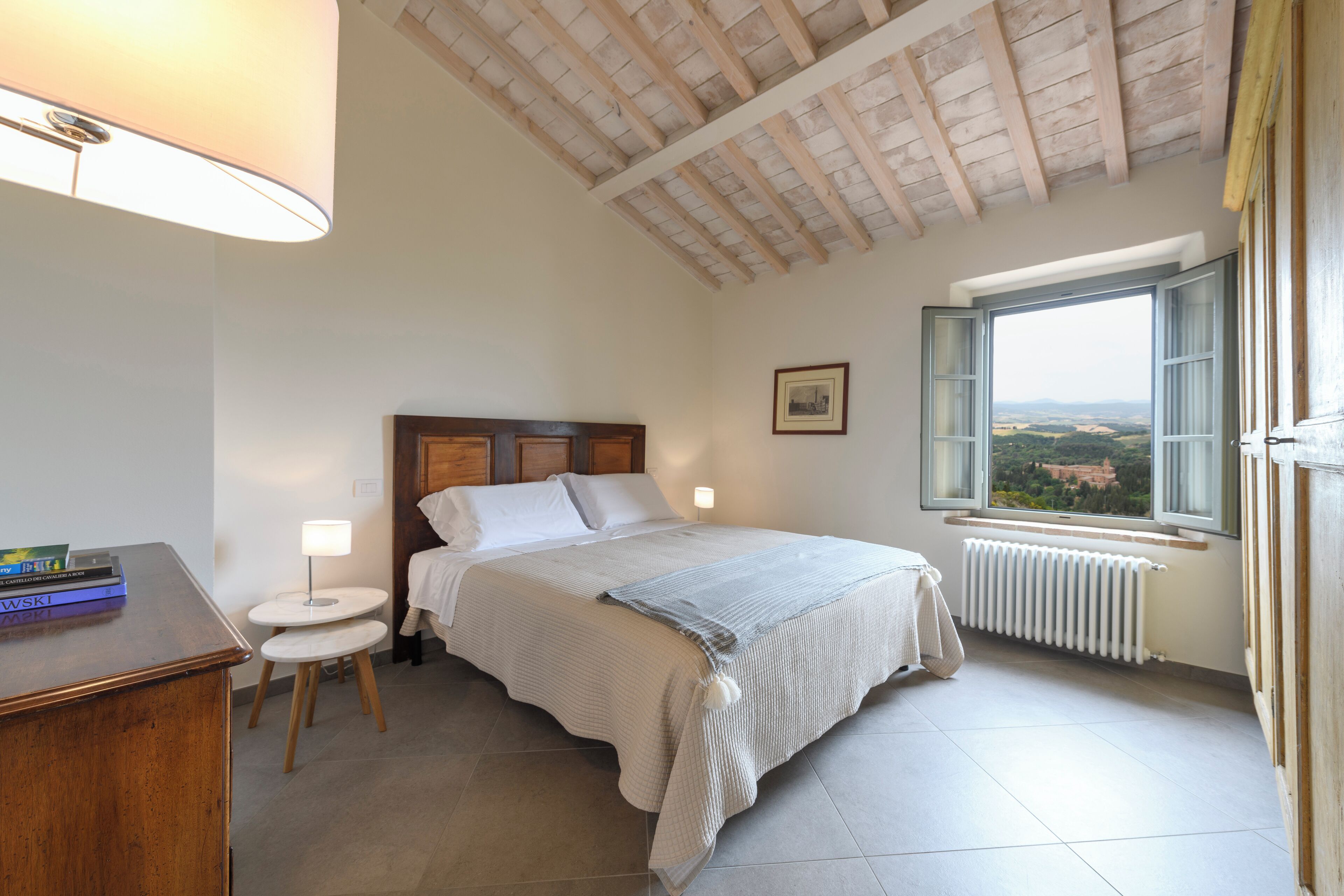 A bedroom with a bed, bedside table, lamp, and a window with a view.