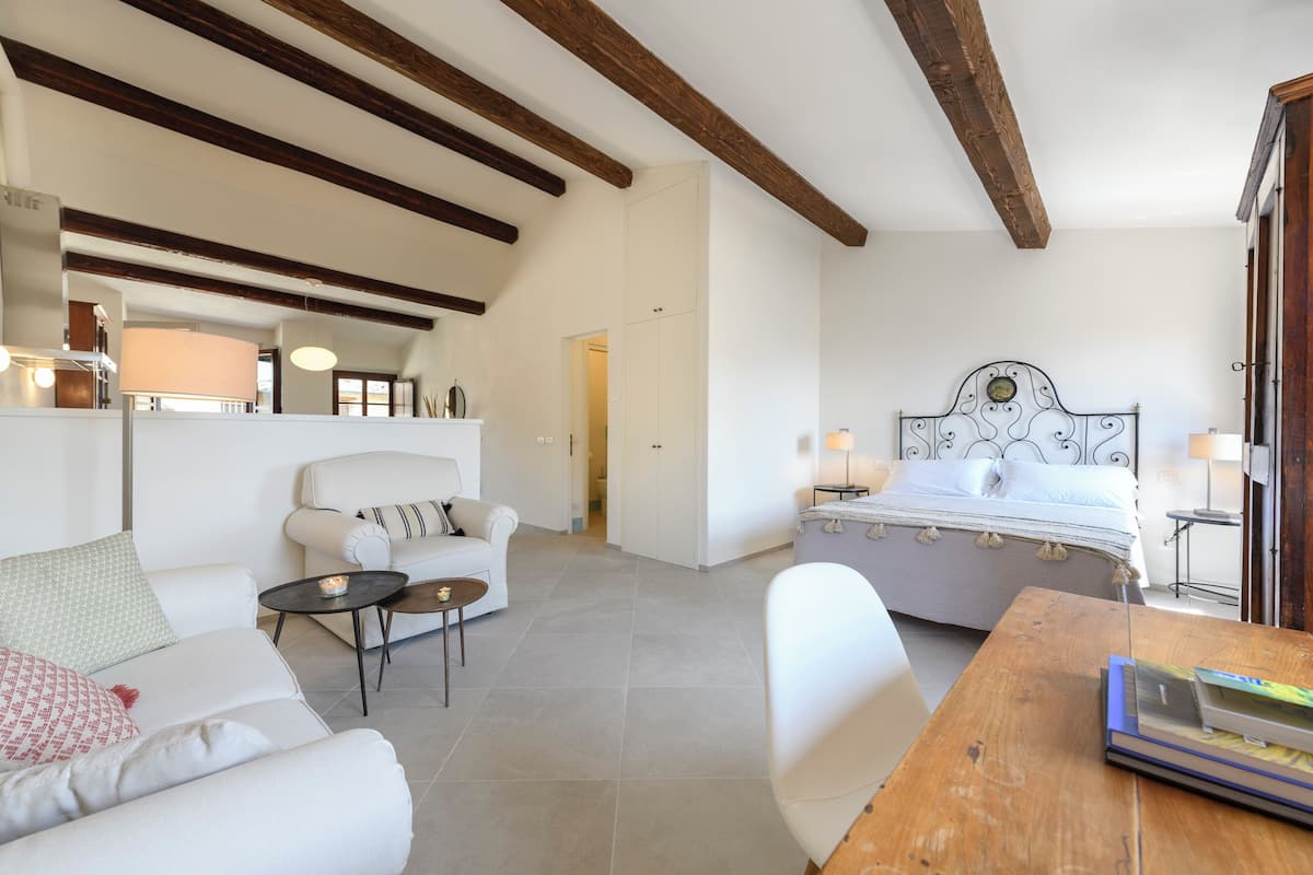 Un dormitorio moderno con una cama grande, una zona de estar con sofá y una mesa de centro, y una mesa de comedor de madera.