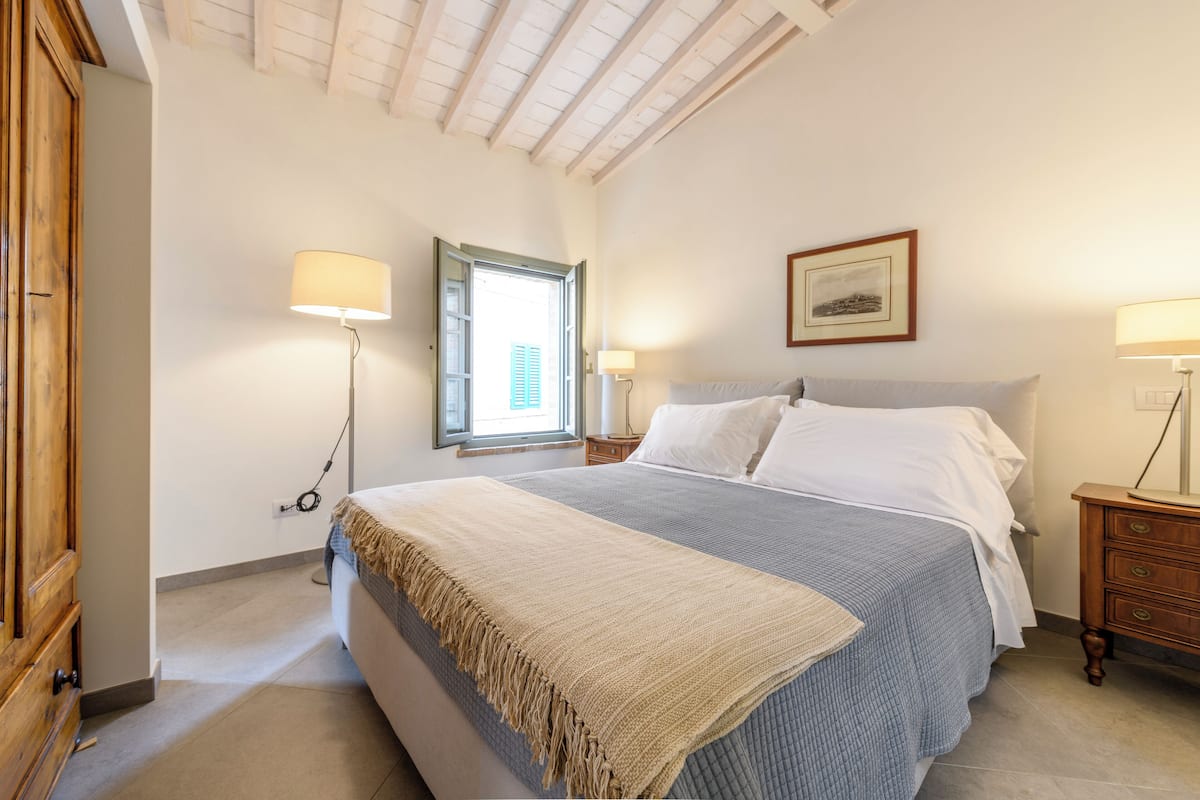 Un dormitorio con cama, lámparas de noche, una ventana y un armario de madera.