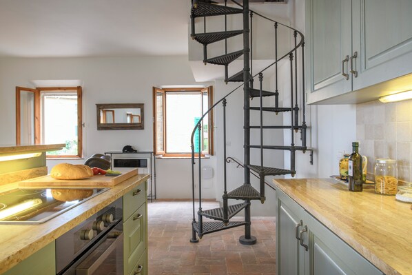 A kitchen with a spiral staircase, a wooden countertop, and a window with a view. - Albergo Diffuso Borgo Santo (Asciano)