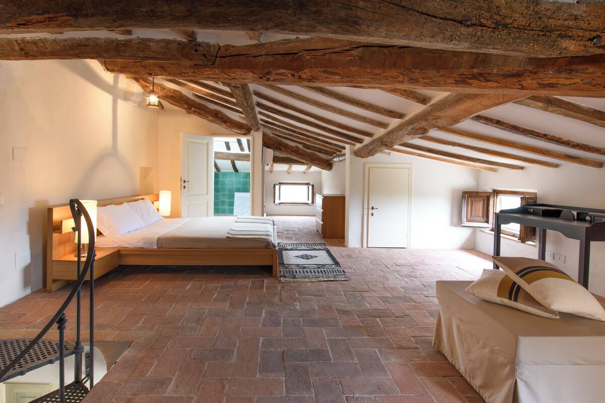 Un dormitorio con techo de madera, cama, escritorio y ventana.