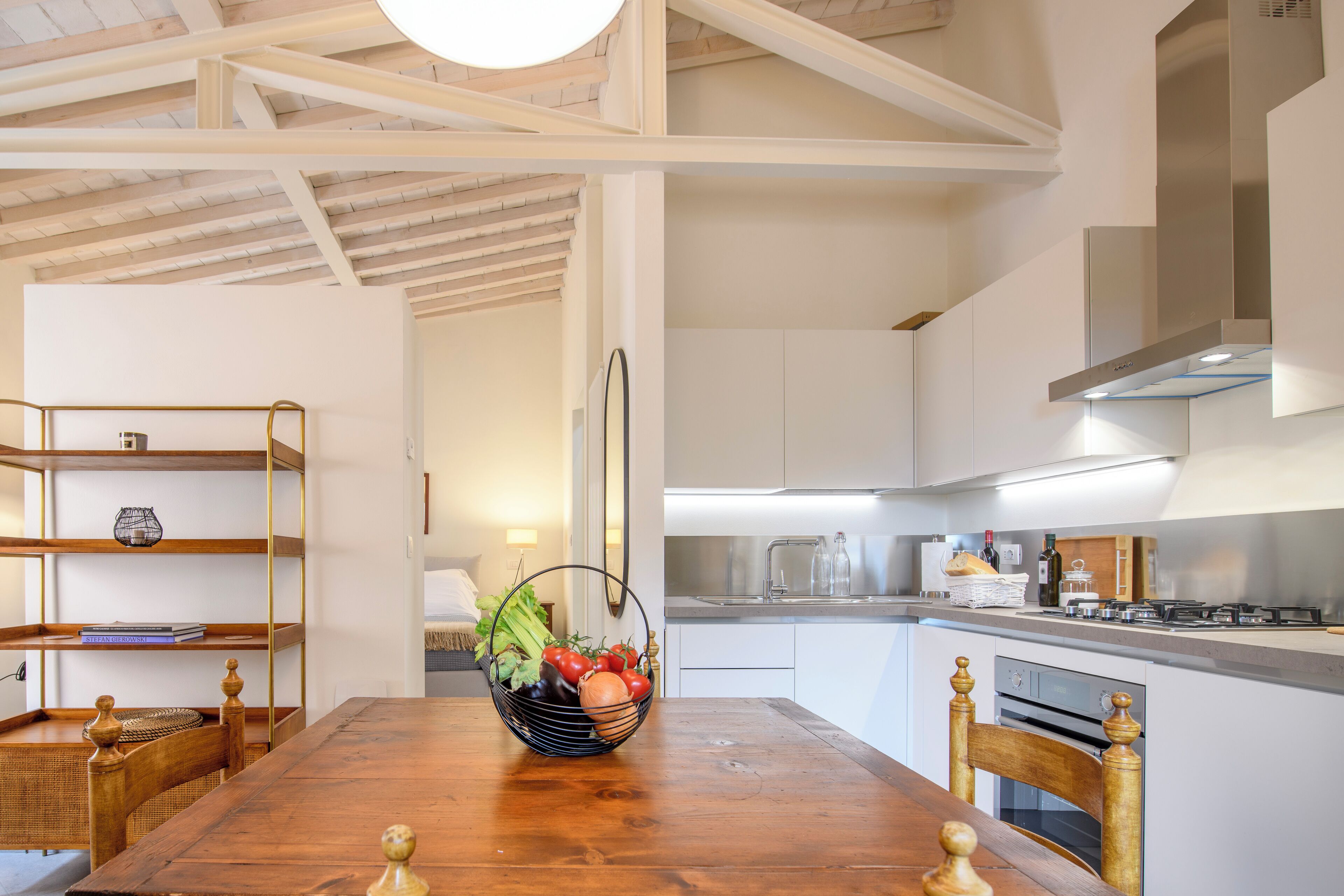 Une cuisine moderne avec des armoires blanches, une hotte en acier inoxydable et une table à manger en bois sur laquelle est posé un panier de fruits.