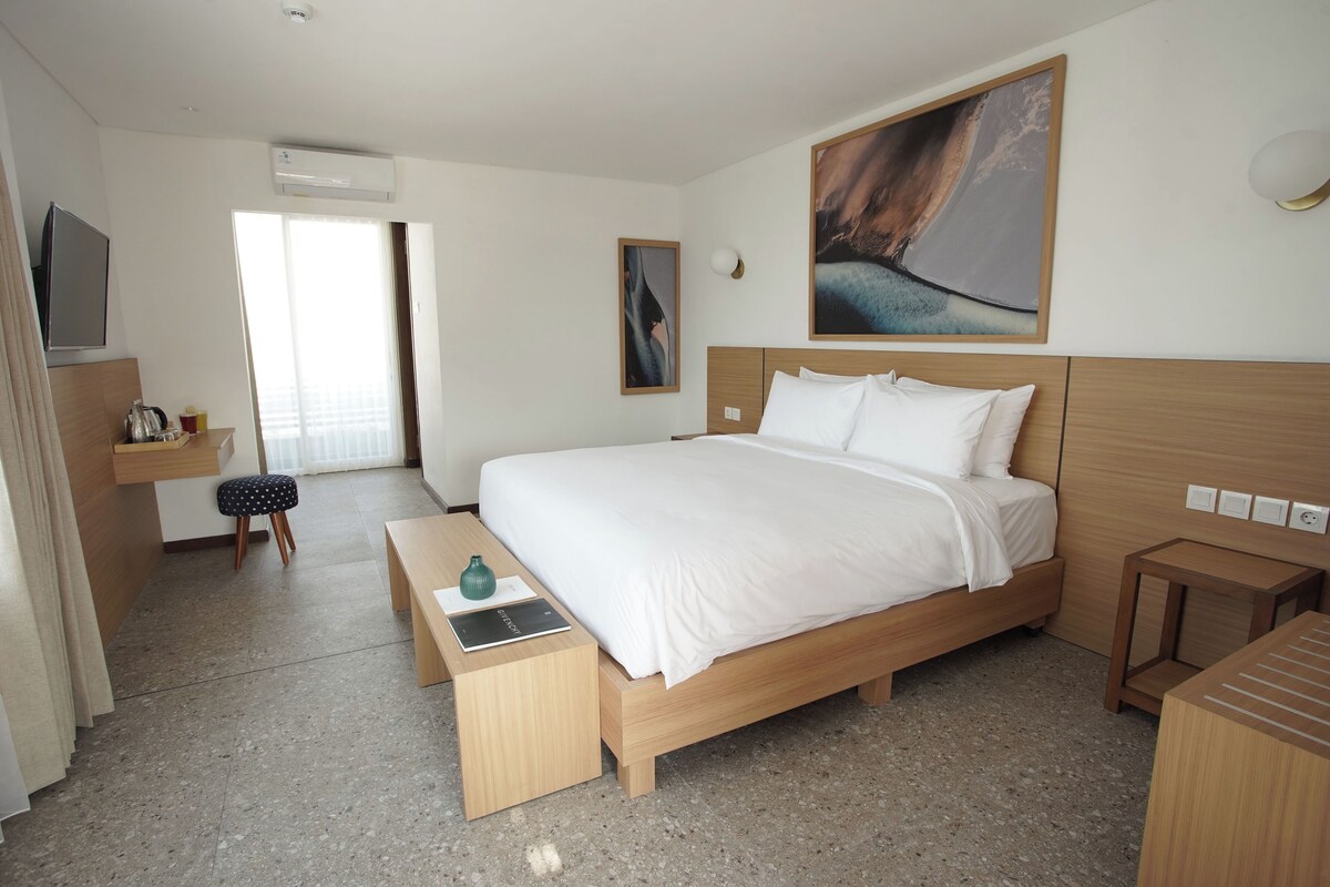 Ein modernes Hotelzimmer mit einem großen Bett, einem Schreibtisch mit Stuhl, einem kleinen Hocker und einer Bank.