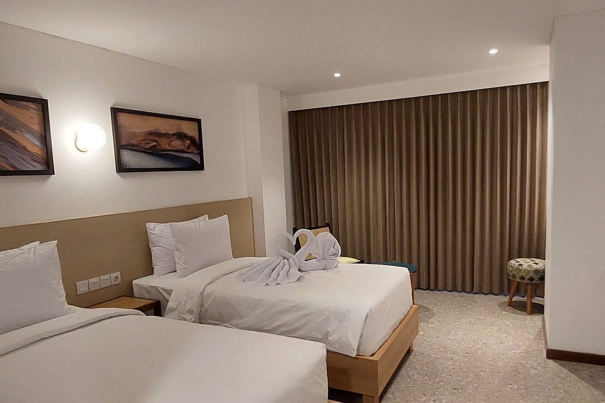 A hotel room with two beds, a small table, and a curtain.