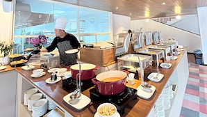 A buffet setup with various food stations, a chef preparing food, and a modern interior with wooden ceiling and large windows. - Gendhis Batu Boutique Hotel (Batu)