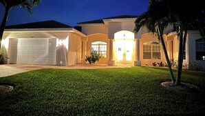 A well-lit residential house with a garage, a front entrance, and a lawn. - Villa Meridian Spacious villa for discerning guests. (Cape Coral)