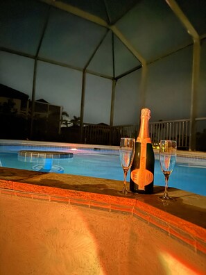 Una botella de champán Brut Rosé y dos copas sobre una mesa junto a la piscina.