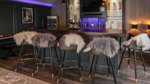 Een moderne keuken met een bar, voorzien van barkrukken met een zachte bekleding, een grote flatscreen-tv en een wijnrek.