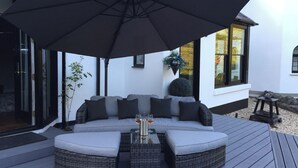 Een modern buitgedeelte met een grote parasol, een bank en een tafel met drankjes.