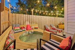 A backyard with a hot tub, lounge chairs, and string lights.