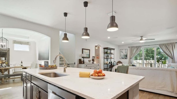 Una cocina moderna con una isla central, iluminación colgante y vistas al salón.