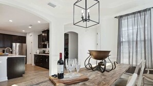 Una cocina moderna con armarios oscuros, un refrigerador de acero inoxidable y una mesa de comedor de madera con una botella de vino y copas.