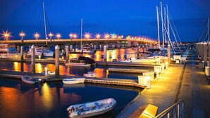 Un puerto deportivo con barcos amarrados, un puente al fondo y un paseo marítimo bien iluminado.