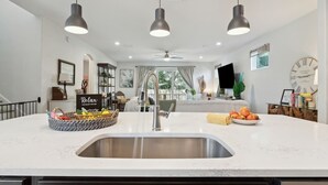 Una cocina moderna con una isla central, luces colgantes y un reloj visible en la pared.
