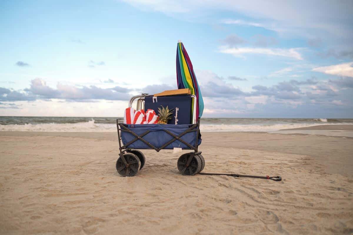 A beach cart with a colorful umbrella and a surfboard on a sandy beach.