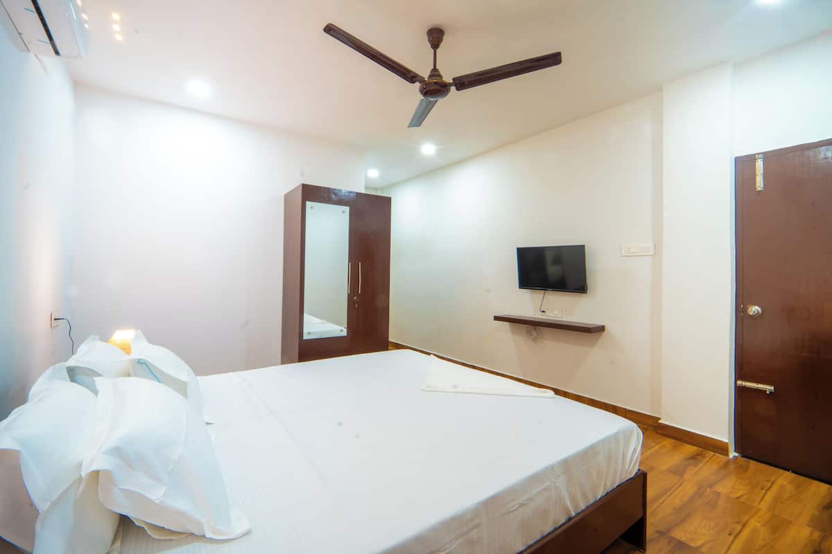 A bedroom with a bed, a ceiling fan, a TV mounted on the wall, and a wooden door.