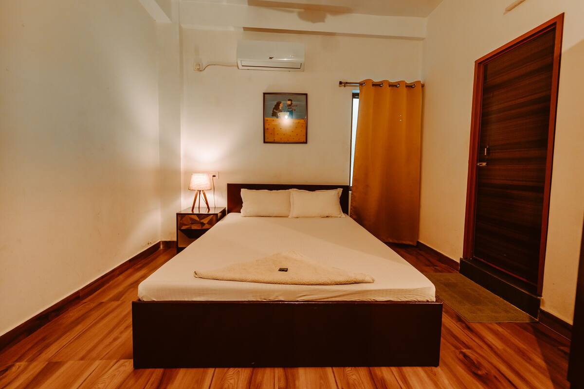 A hotel room with a bed, a nightstand, a lamp, a picture on the wall, and a door.