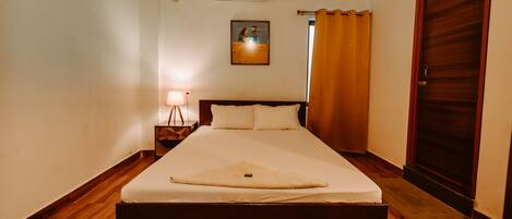 A hotel room with a bed, a nightstand, a lamp, a picture on the wall, and a door.