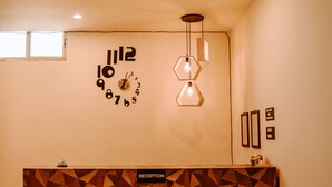 Una zona de recepción con un muro de diseño geométrico, un reloj y lámparas colgantes.