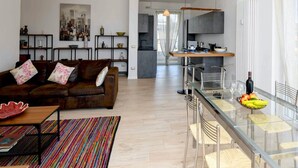 A modern living room with a brown leather sofa, a glass dining table with chairs, and a colorful rug.