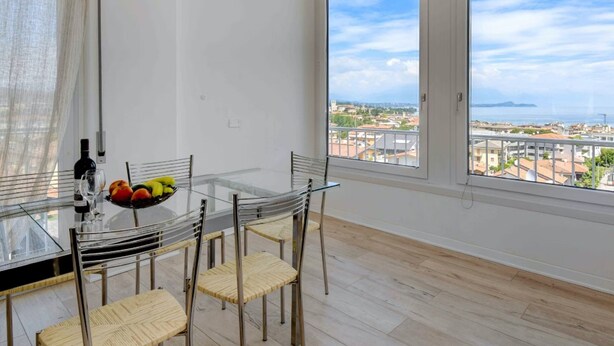 A dining area with a glass table and chairs, a bowl of fruit, and a bottle of wine on the table.