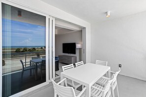 A balcony with a white table and chairs, a TV, and a view of the ocean. - Luxury Condo Resort on the Beach (Treasure Island)