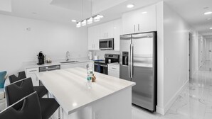 A modern kitchen with white cabinetry, stainless steel appliances, and a central island with seating. - New Tropical Resort Living on the Beach (Treasure Island)