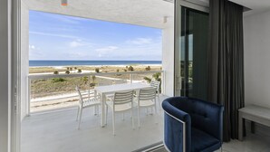 Ein Balkon mit einem weißen Tisch und Stühlen, einem blauen Sessel und Blick auf Strand und Meer.