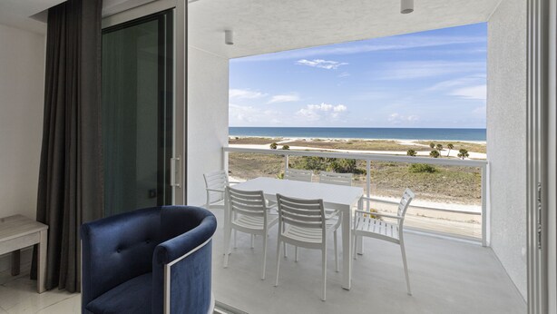 Un balcón con una mesa y sillas blancas, una silla azul, y vista al mar.