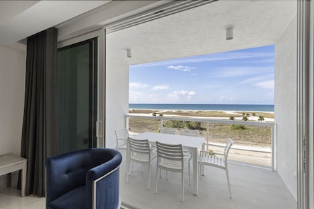 A balcony with a white table and chairs, a blue chair, and a view of the beach.