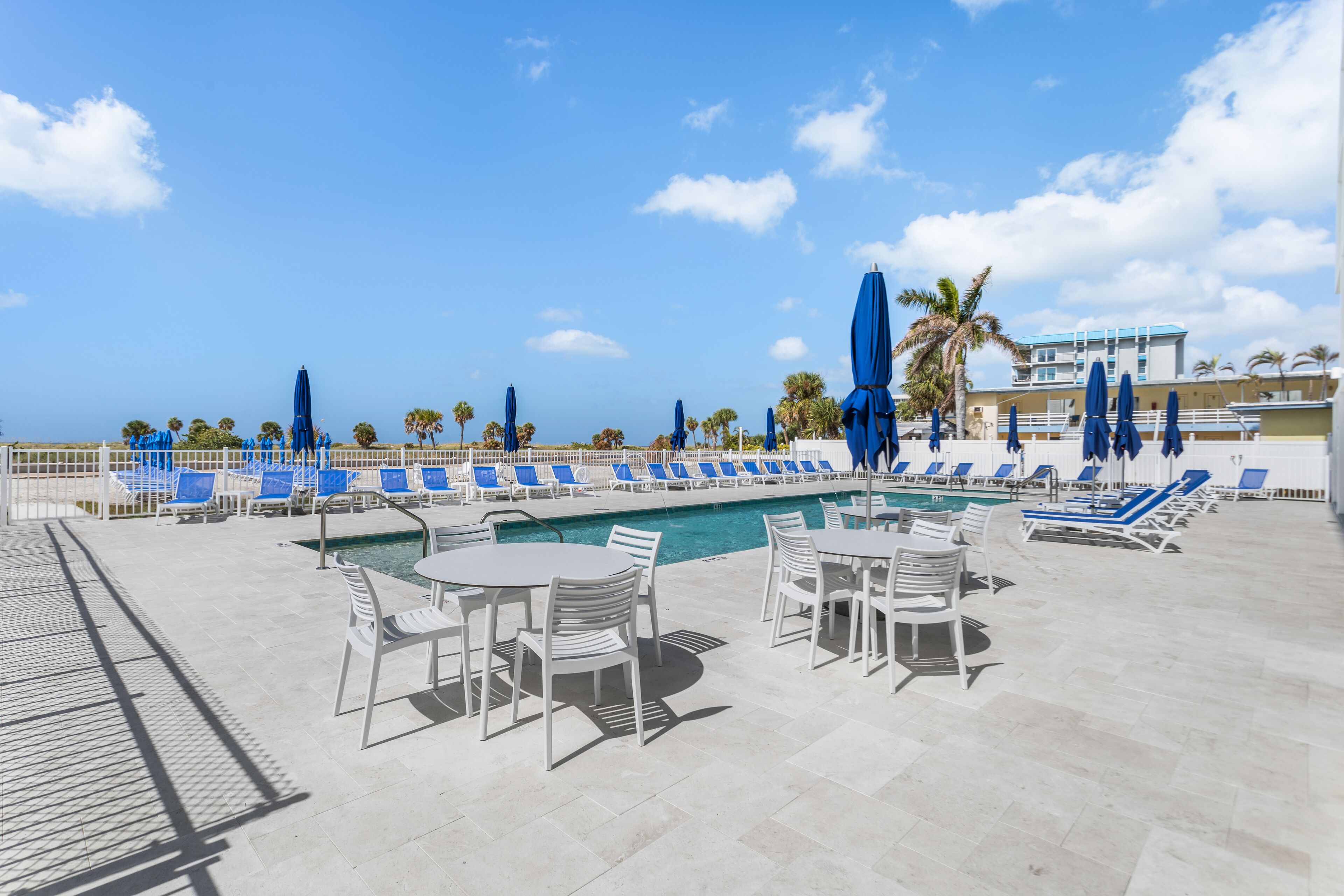 A poolside area with lounge chairs and umbrellas, a pool, and a building in the background.