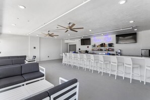 Een moderne bar met witte barkrukken, een neonbord met de tekst 'Ocean Club' en plafondventilatoren.
