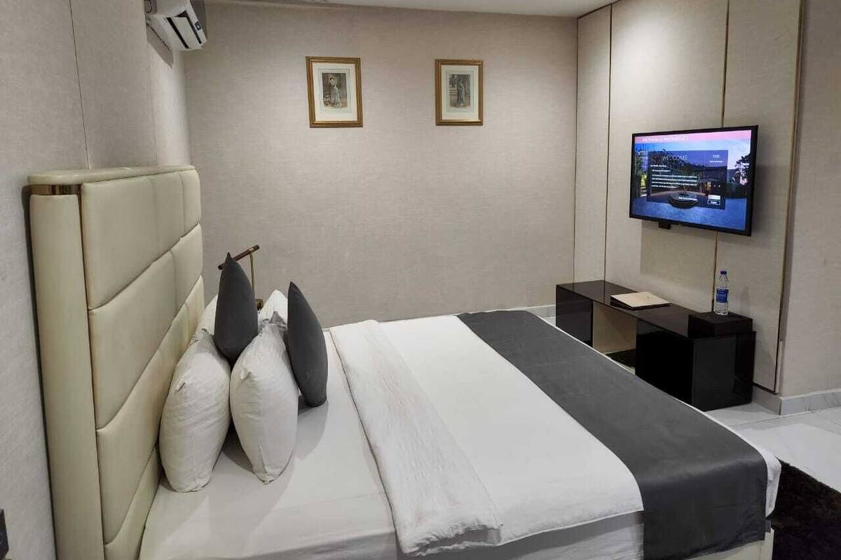 A modern hotel room with a large bed, a flat-screen TV, and a small bedside table.