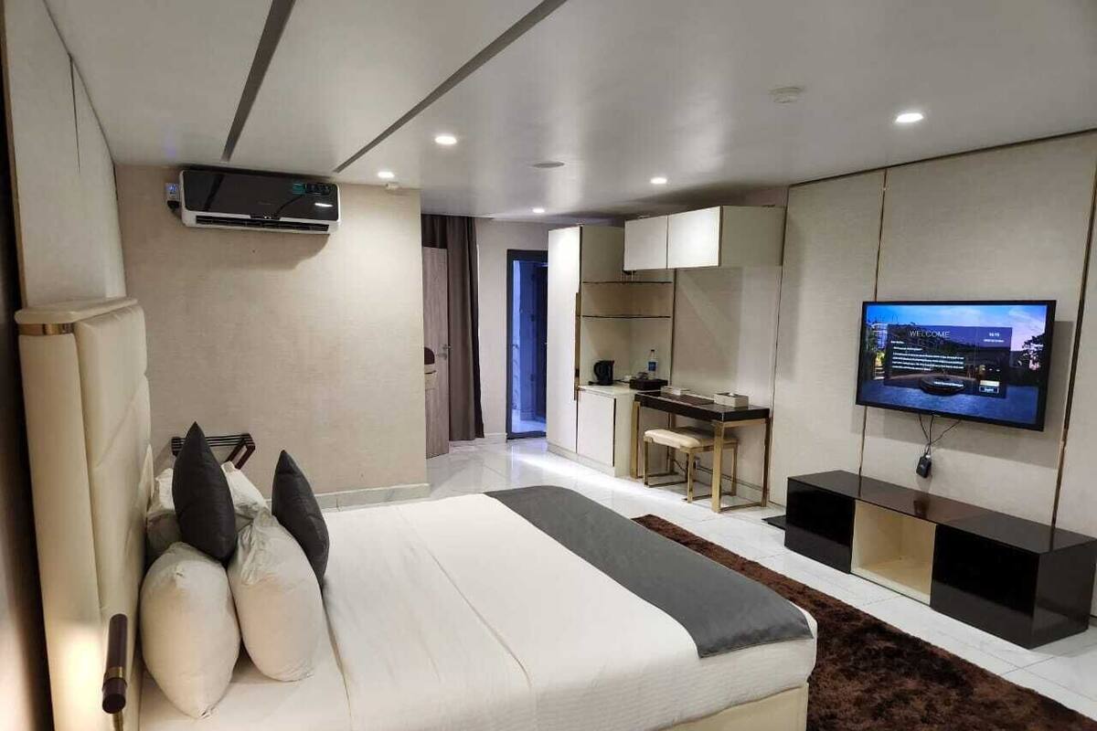 A modern bedroom with a large bed, a TV, and a kitchenette.