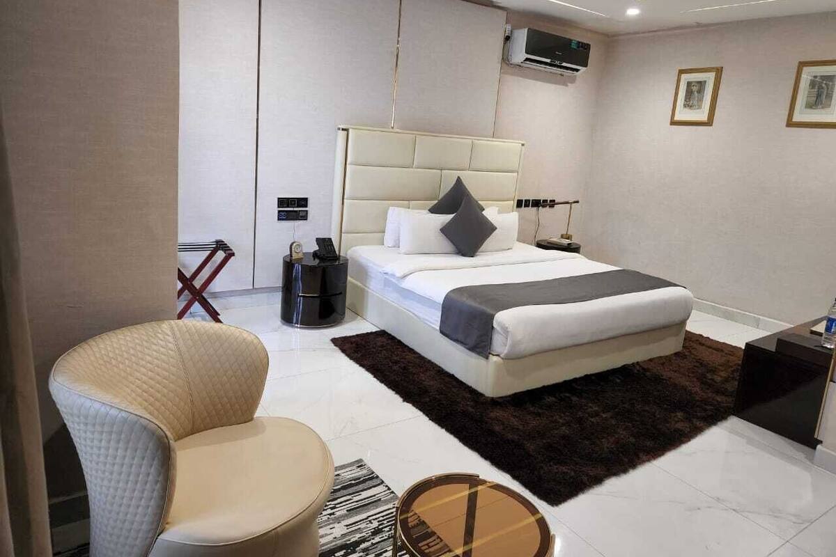 A modern hotel room with a large bed, a bedside table, a chair, and a small side table.