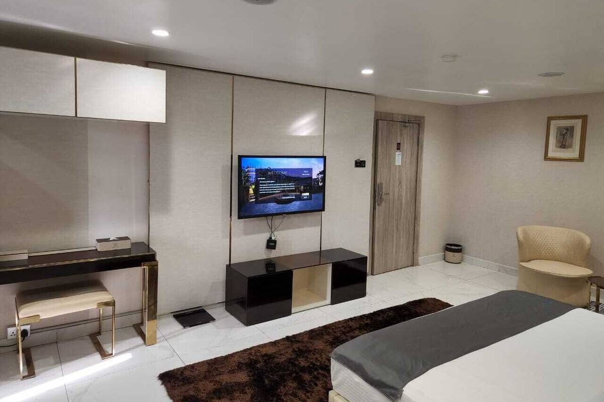 A modern hotel room with a flat-screen TV mounted on the wall, a desk with a chair, a bed with a headboard, and a sofa.