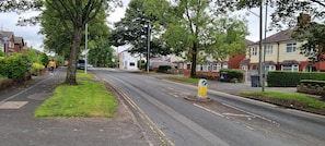 A residential street with houses on both sides, a sidewalk, and a road with a blue traffic sign. - Corner Shop Apartments Sleeps 5 Parking (Stoke-on-Trent)