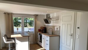 Een moderne keuken met een houten aanrecht, een inbouwoven en een spoelbak. Er is een raam met gordijnen en uitzicht op bomen.