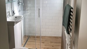 Een moderne badkamer met een douchecabine van glas, witte metro tegels, een houten vloer, een wastafel en een handdoekhouder.