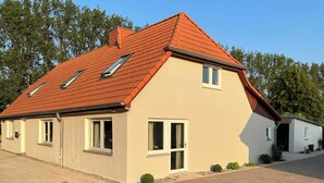Een modern herenhuis met twee verdiepingen, een rode dakbedekking van tegels, veel ramen en een verharde oprit.