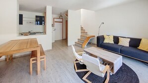 Un salon moderne avec une table à manger en bois, un canapé noir agrémenté de coussins jaunes, un fauteuil blanc et un escalier menant à un deuxième étage.