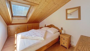 Une chambre avec un plafond en pente, un cadre de lit en bois et un puits de lumière.