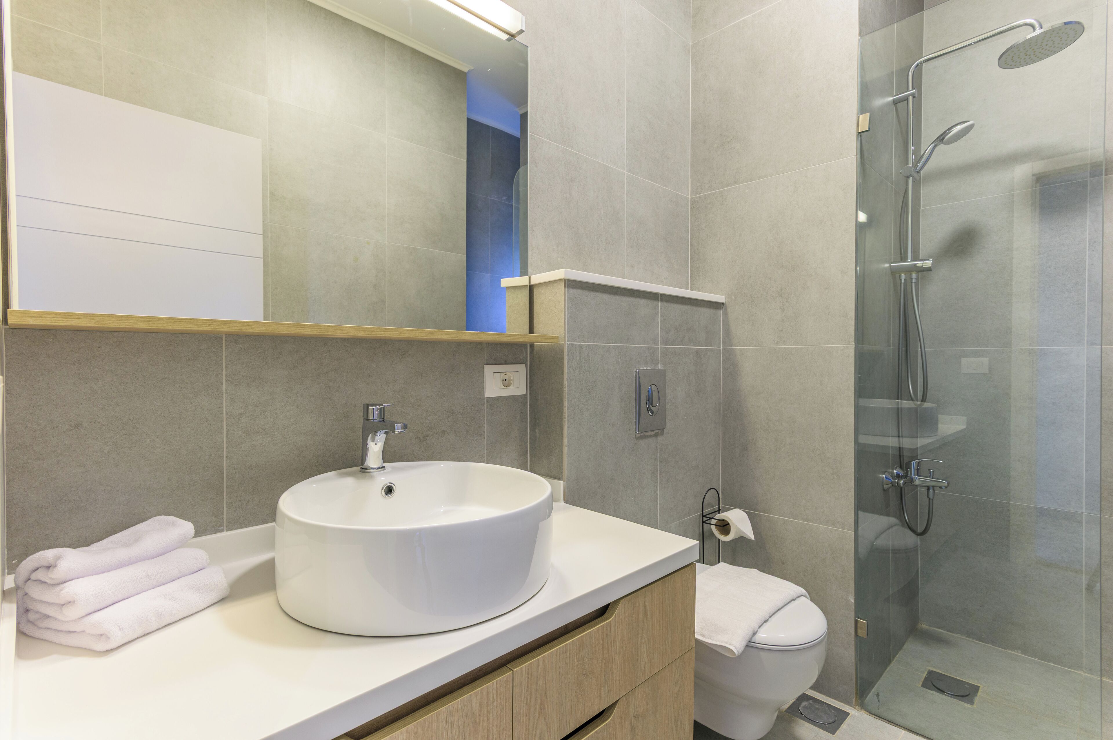 Een moderne badkamer met een rond wastafel, toilet en een douche met glazen wanden.