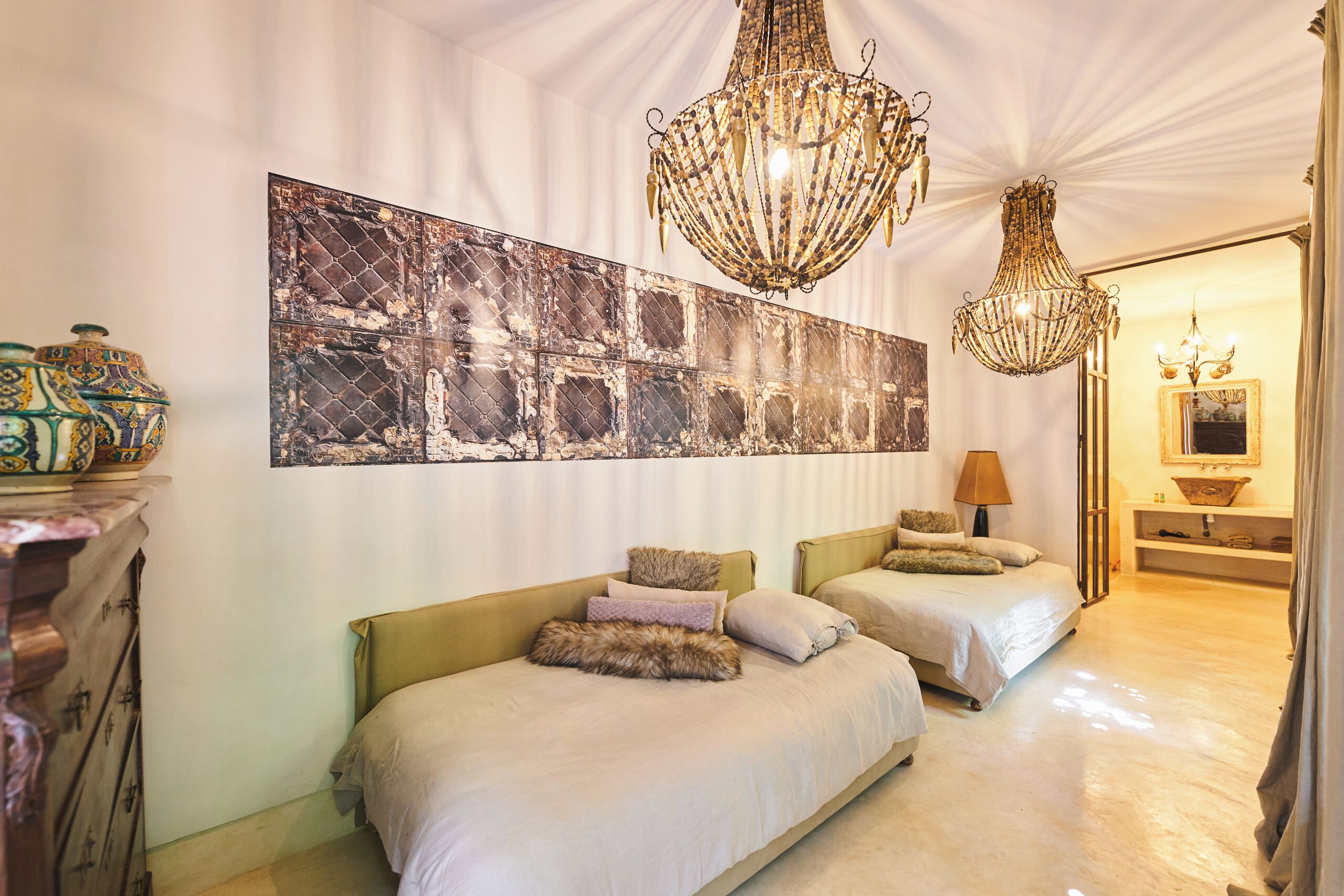 A hotel room with two beds, a large abstract painting, and two chandeliers.