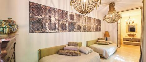 A hotel room with two beds, a large abstract painting, and two chandeliers.