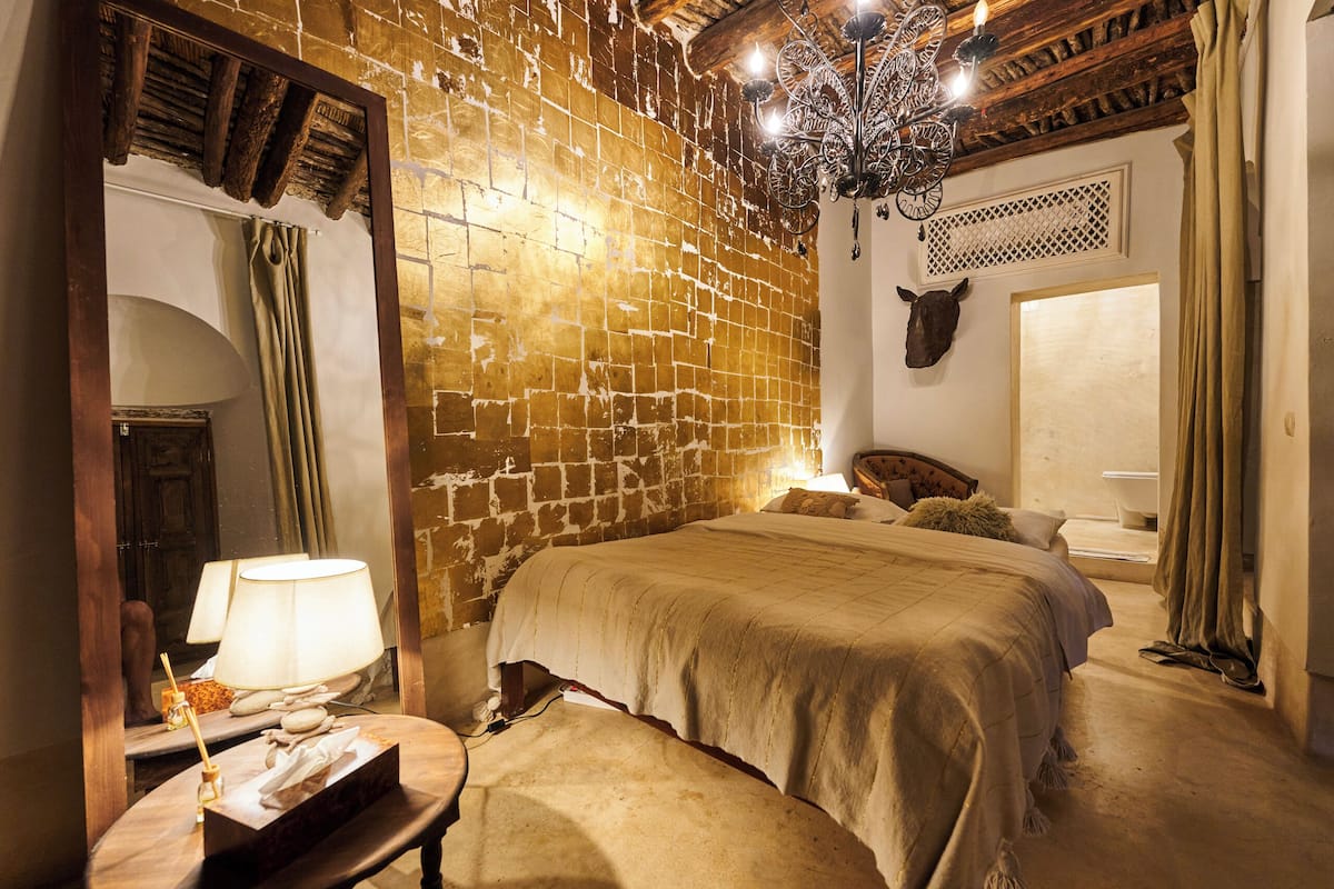 A room with a brick wall, a bed, a chandelier, and a cow head decoration.
